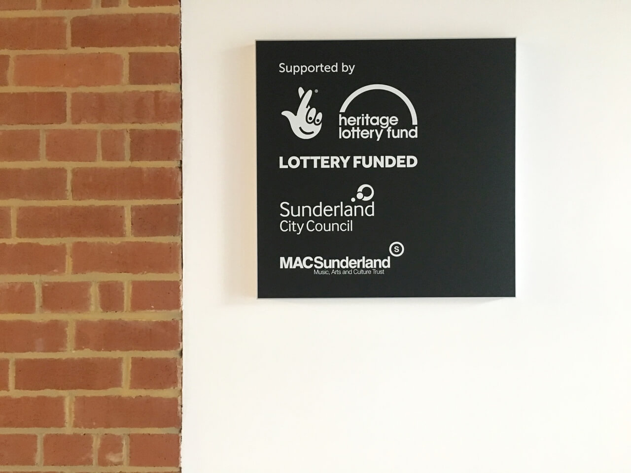 A black sign highlighting supporting bodies logos for Sunderland Council and the lottery fund